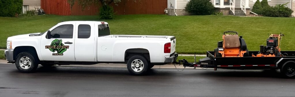 Lawn mowing work truck with Tiger Stripe Lawn Care logo pulling trailer carrying 2 mowers.